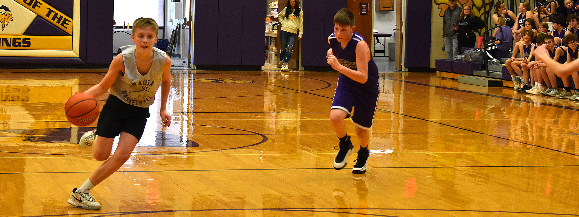 Two boys playing basketball on court with crowd watching.