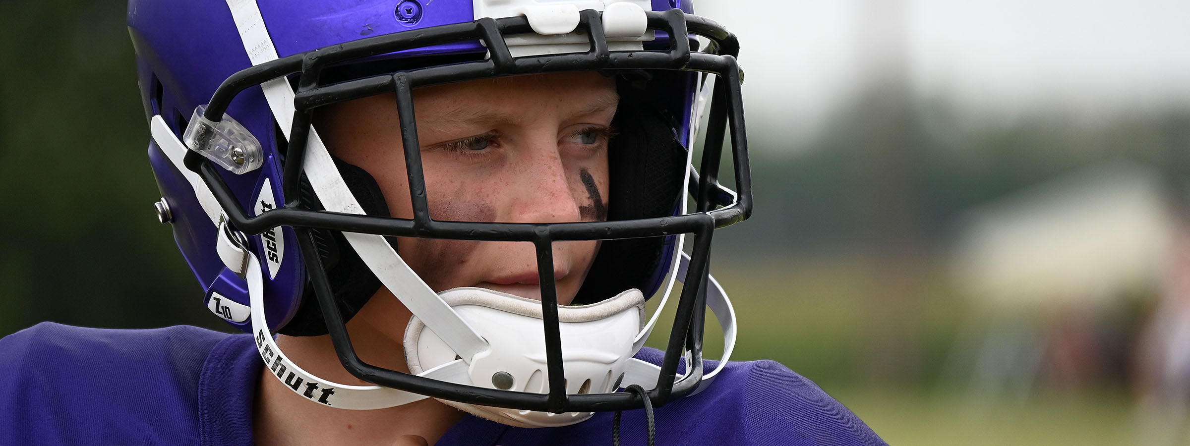 A young man in a purple uniform and helmet stands confidently, ready for action in a dynamic environment.