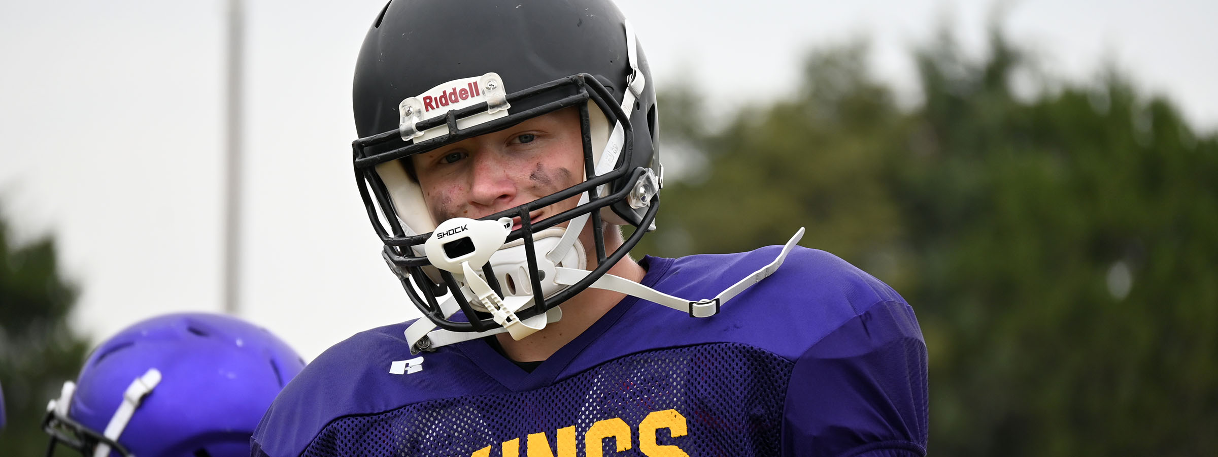 A football player in a helmet and uniform stands ready on the field, showcasing athleticism and team spirit.