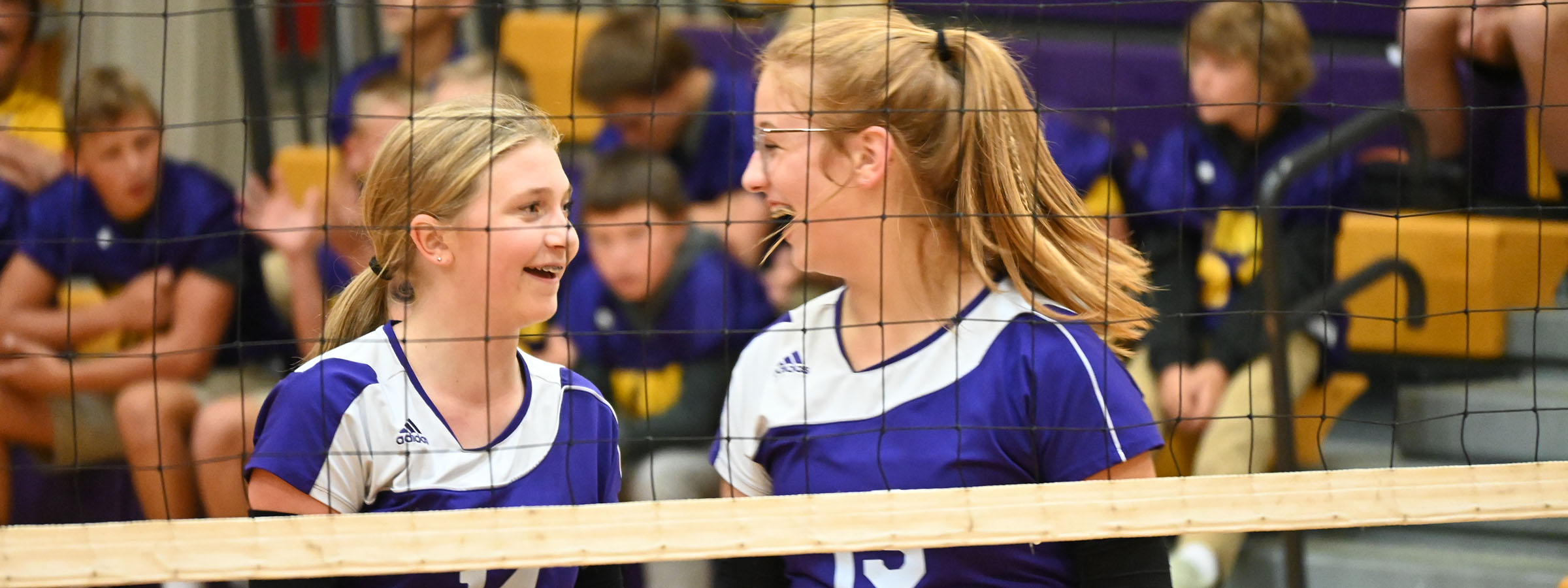 Two girls in purple and white uniforms smiling at each other.