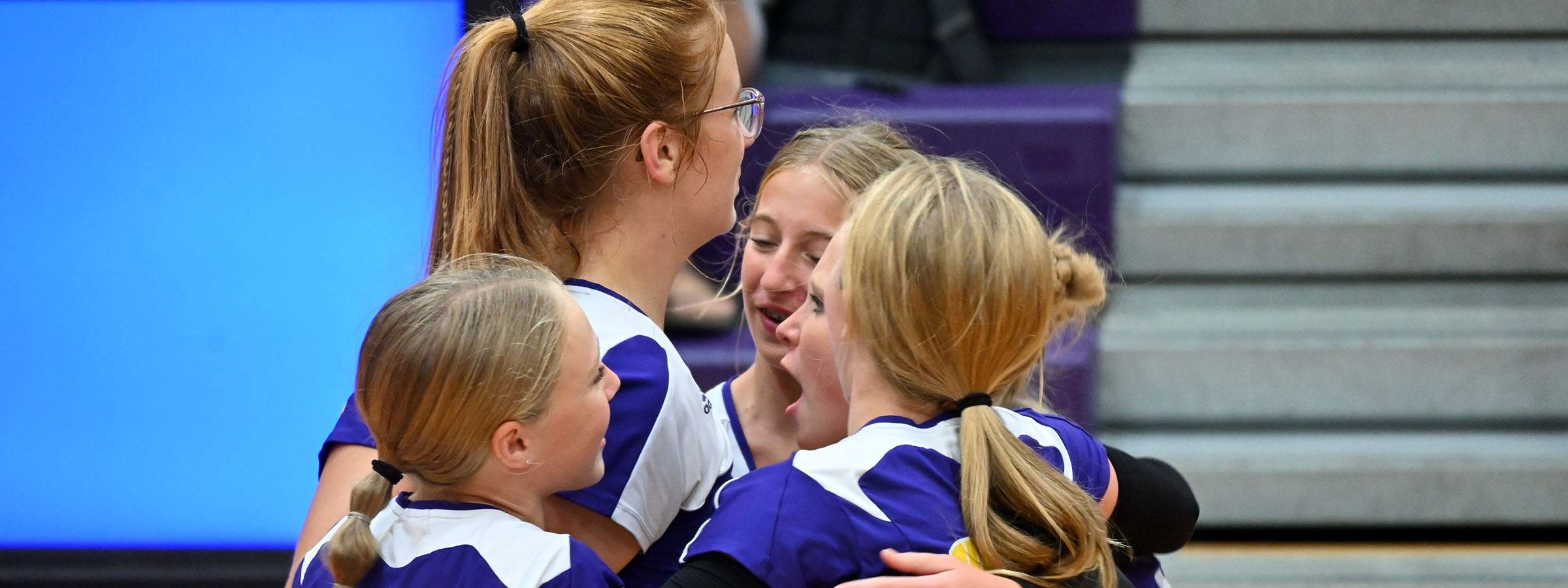 Group of female volleyball players embracing in celebration after winning a match.