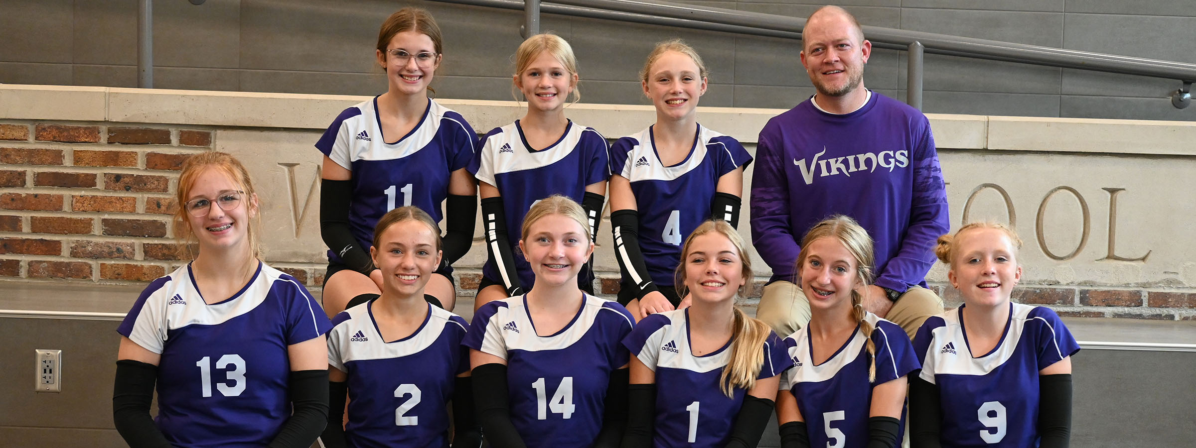 A volleyball team smiling and posing for a group photo on the court.