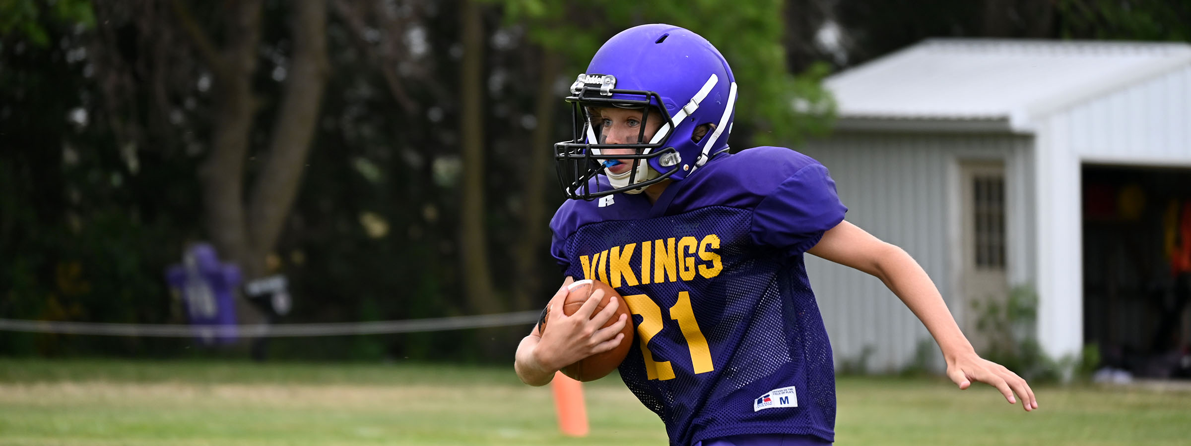 A young boy in a purple uniform running with a football.