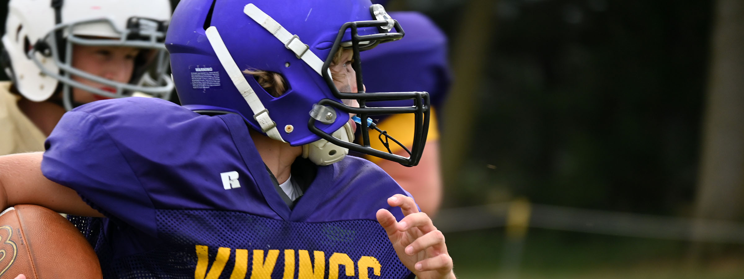 Football player in purple helmet and uniform running with ball on field.