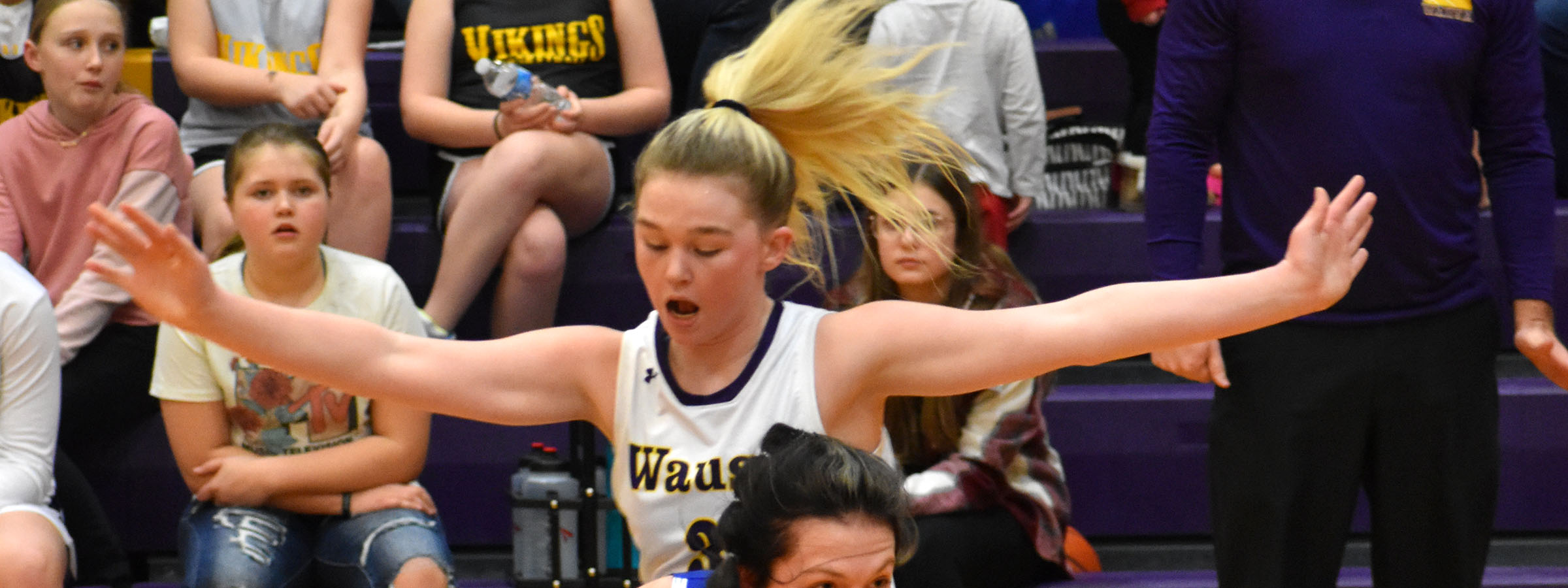 Two girls playing basketball in front of a cheering crowd at a sports event.