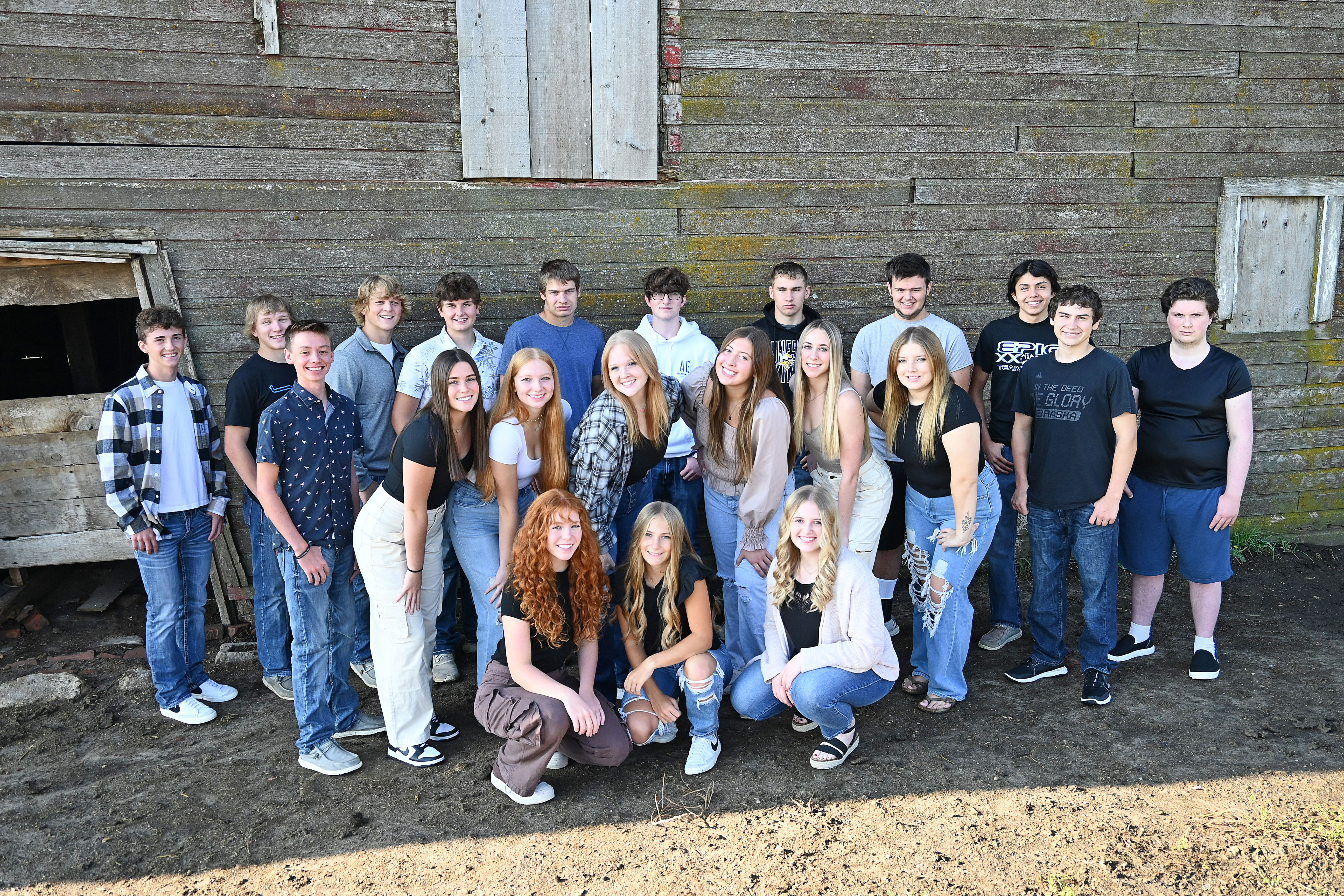 A group of young people smiling in front of a rustic barn, posing for a photo on a sunny day.