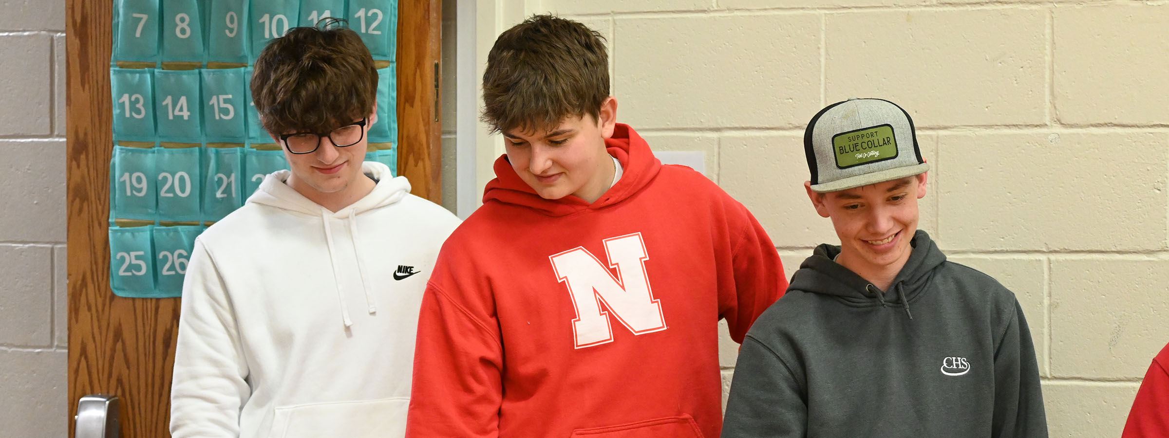 Three boys in hoodies and hats standing in a hallway.