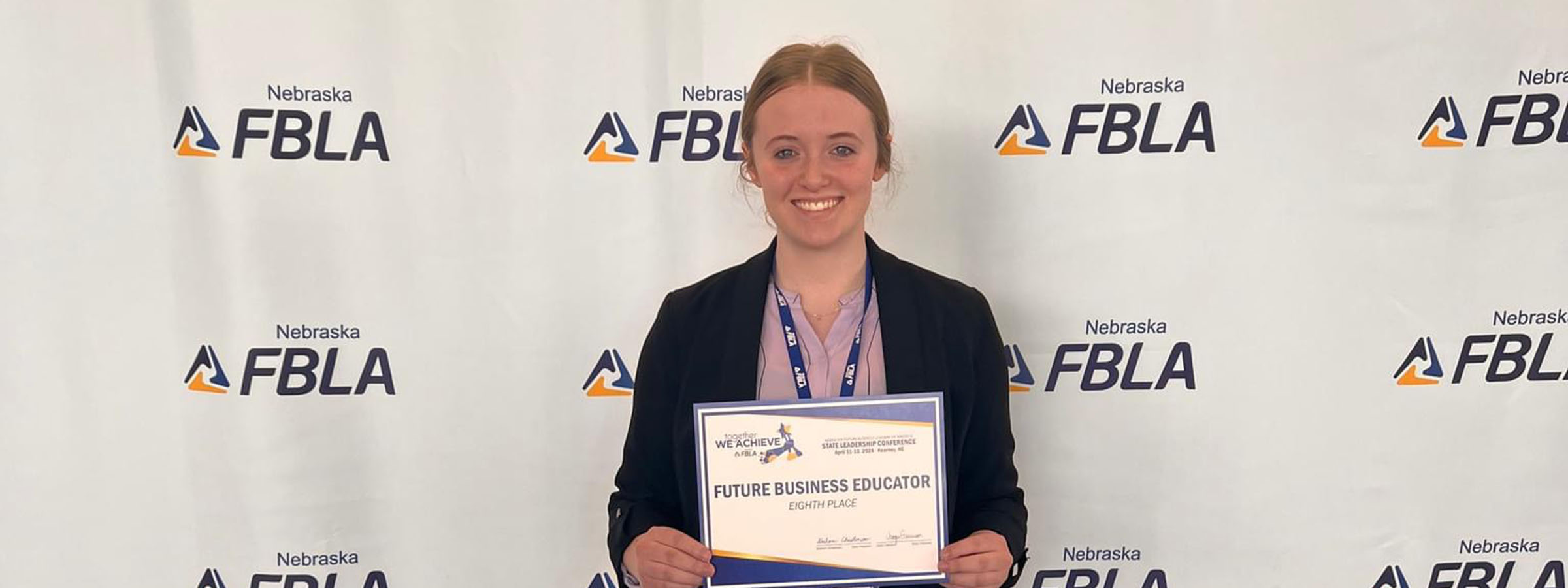 A woman proudly holds a certificate in front of a wall.