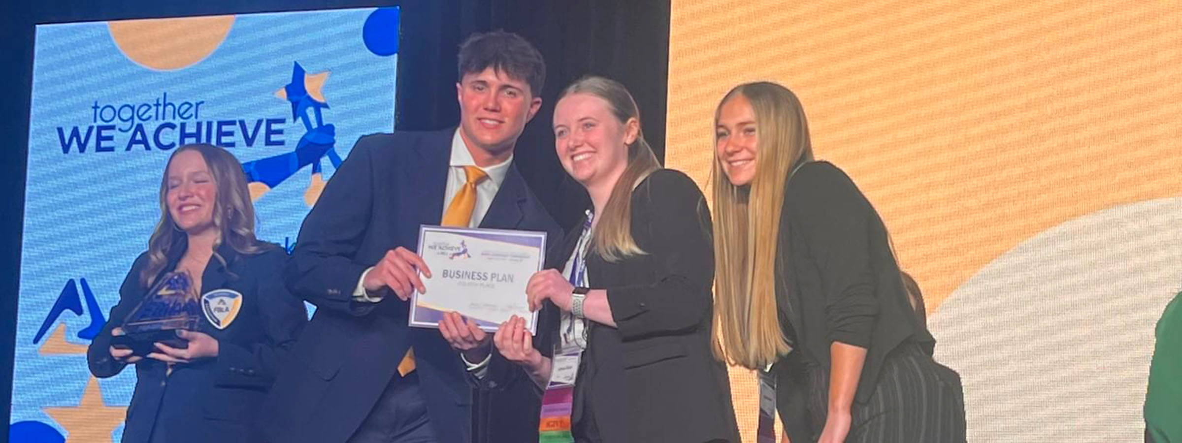  Three people smiling on stage, holding a certificate.