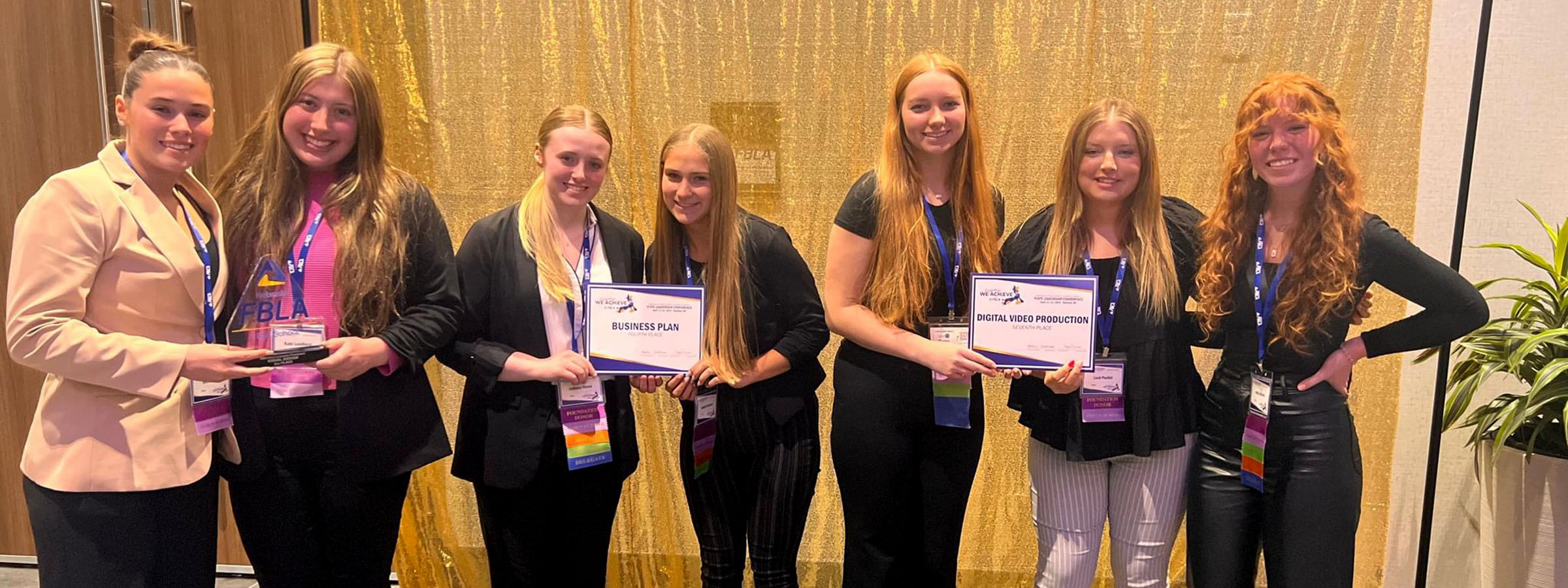 Seven girls proudly displaying a certificate in front of a gold curtain.