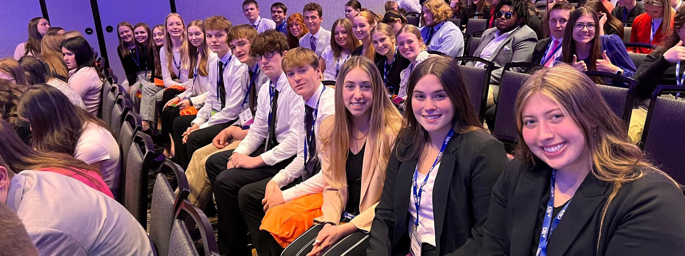 A diverse group of people sitting in a large auditorium, listening attentively to a speaker on stage.