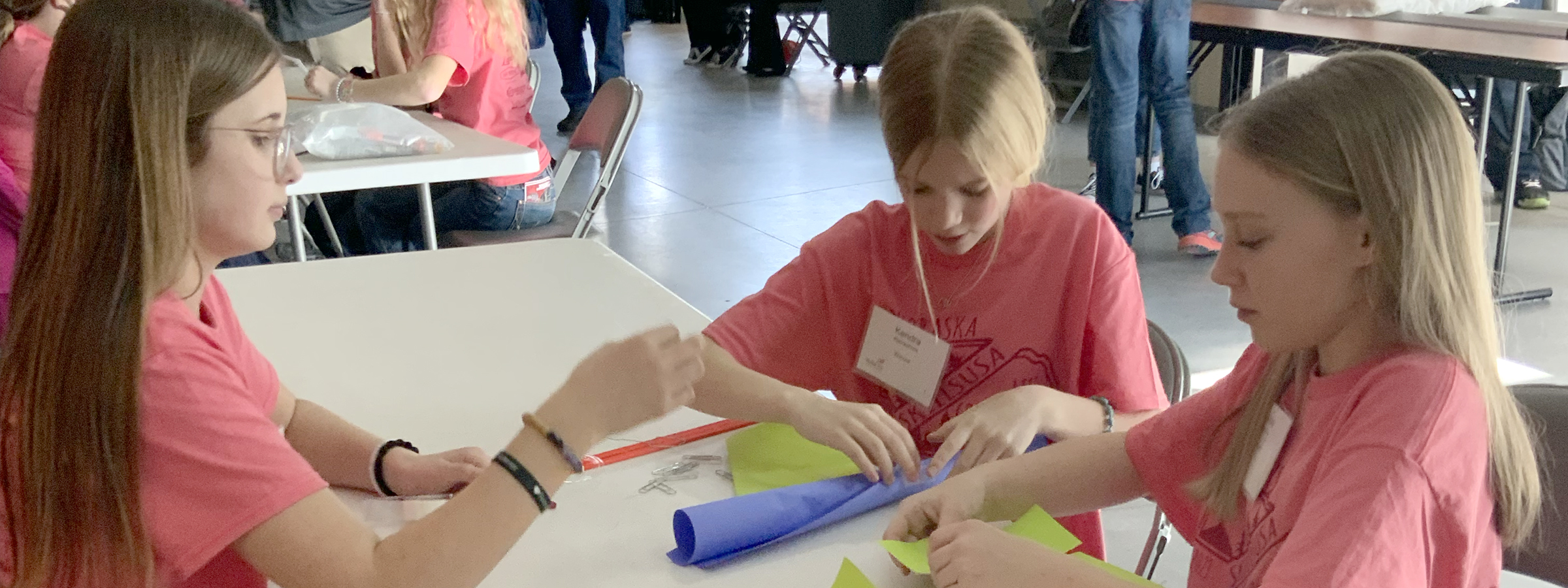 Two girls in pink shirts are focused on their work, collaborating on a paper together at a table.