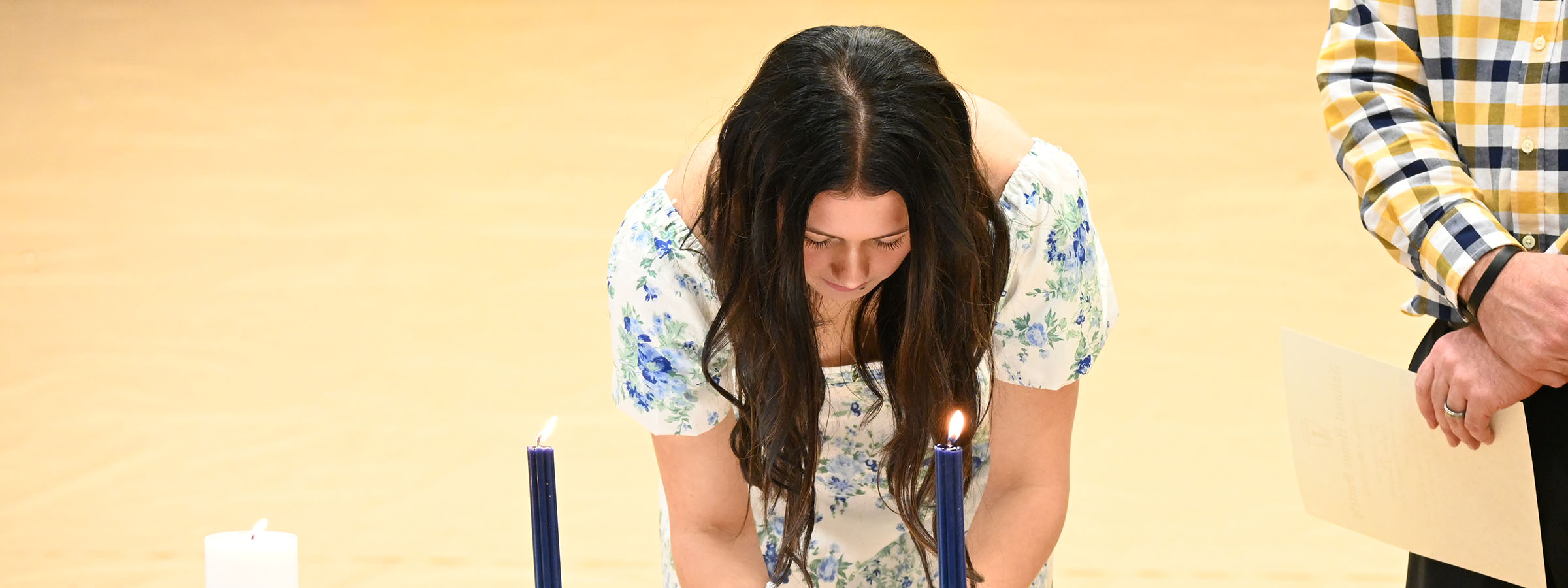 At a ceremony, a woman carefully lights a candle, bringing warmth and light.