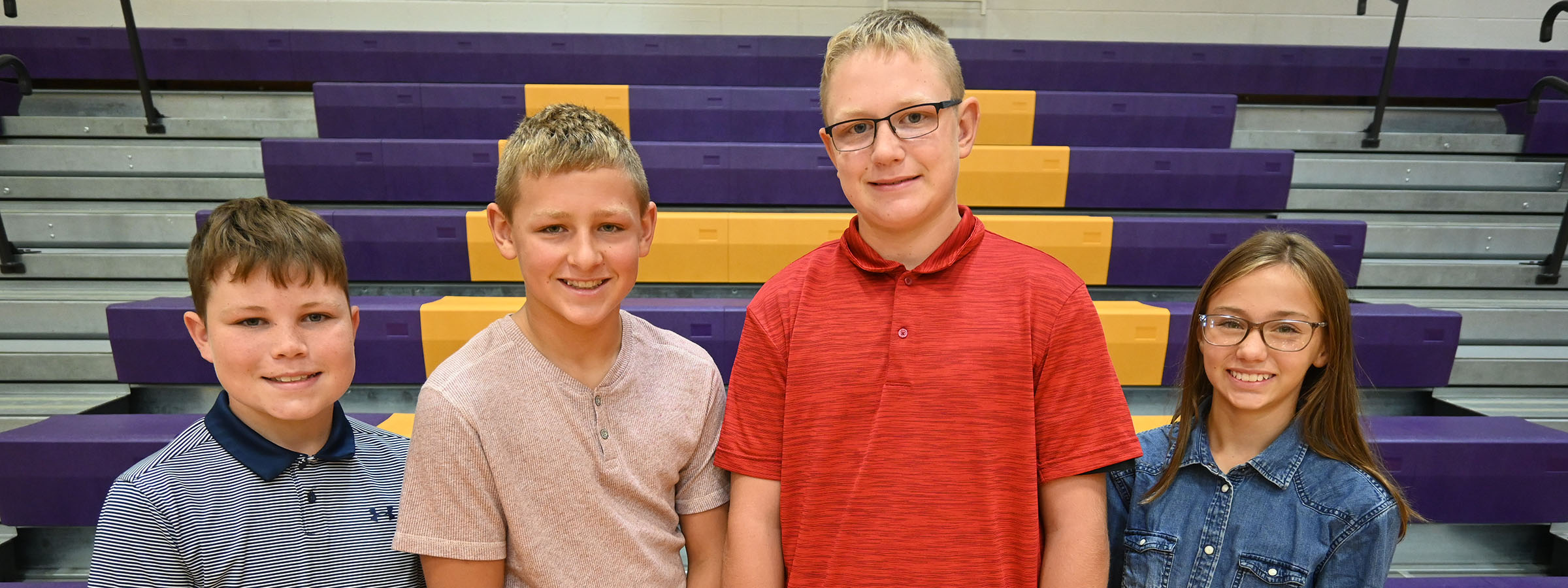 Four young friends posing in front of bleachers at a sports event.