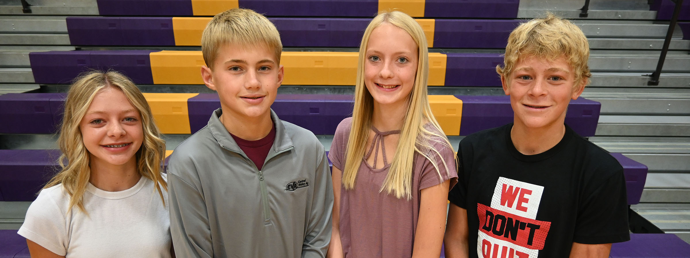 Four young friends posing in front of bleachers at a sports event.