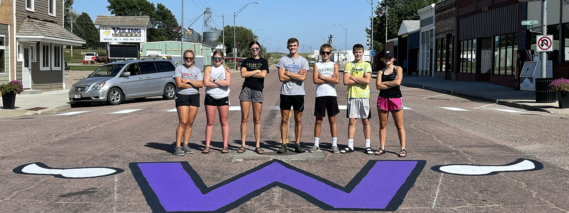  A diverse group of people standing in front of a painted letter 'W'.