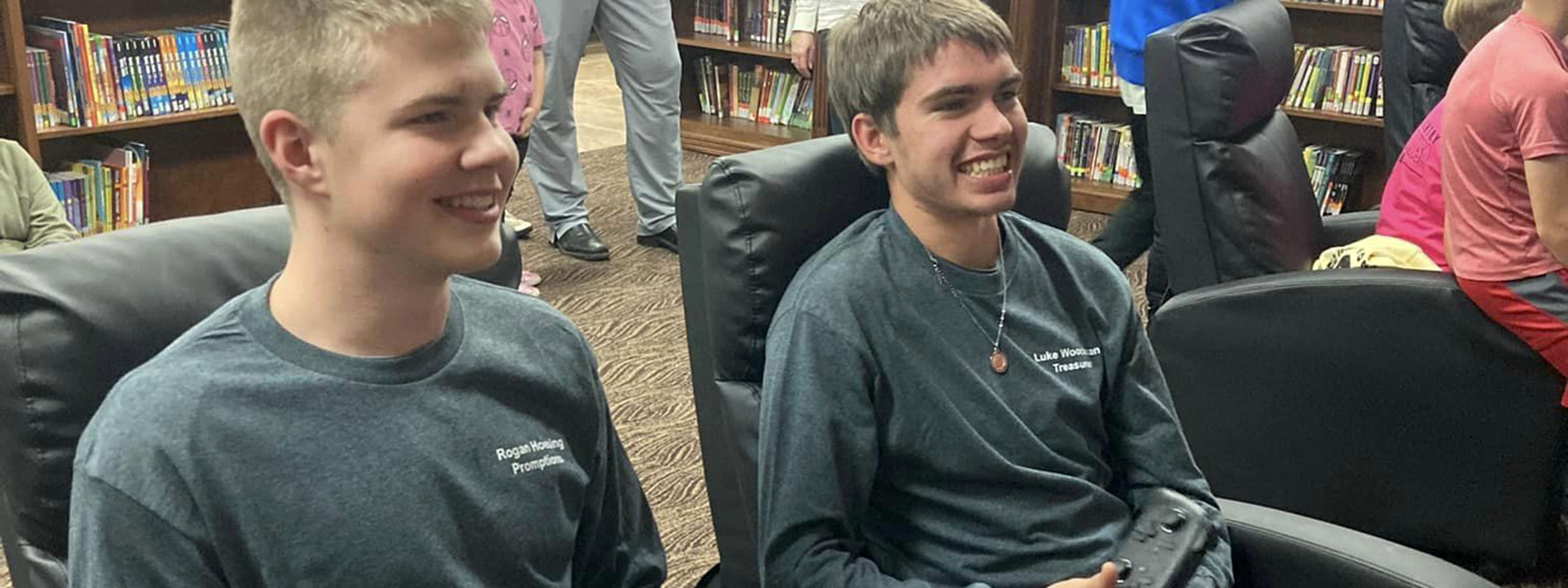 Two boys sitting in chairs, reading books in a library.