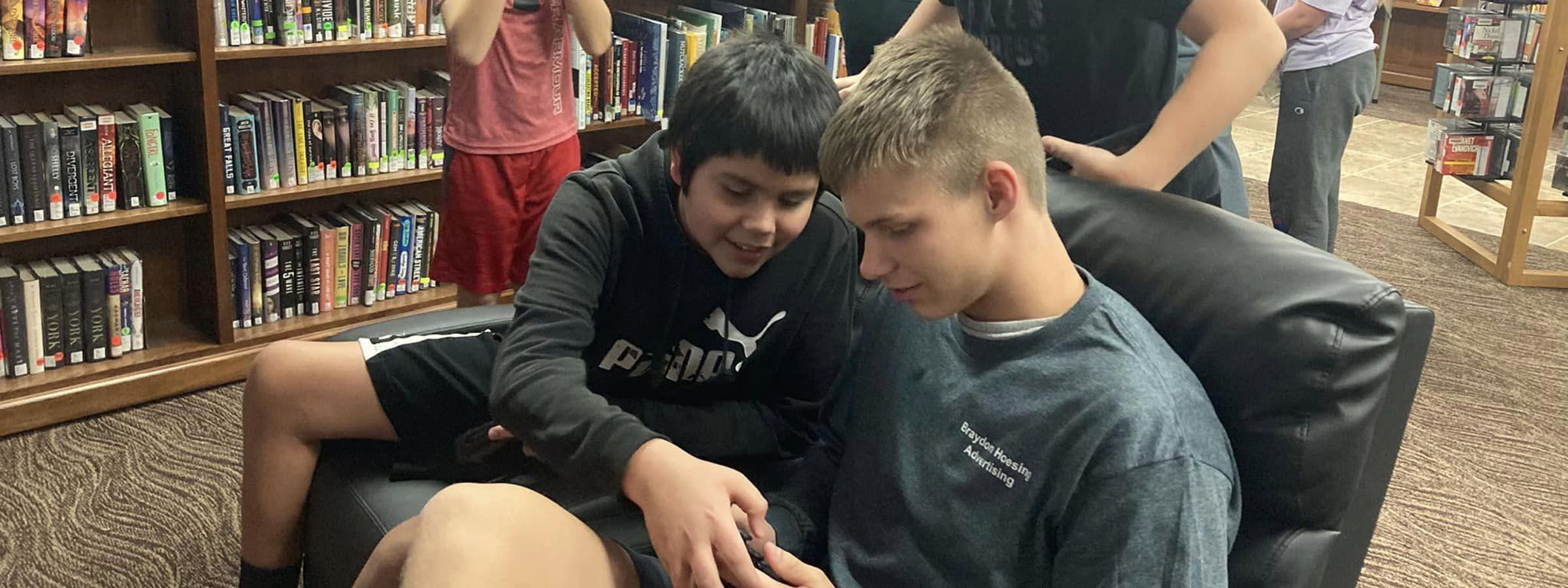 Two boys relax on a couch in a cozy library, surrounded by shelves filled with books and a warm, inviting atmosphere.