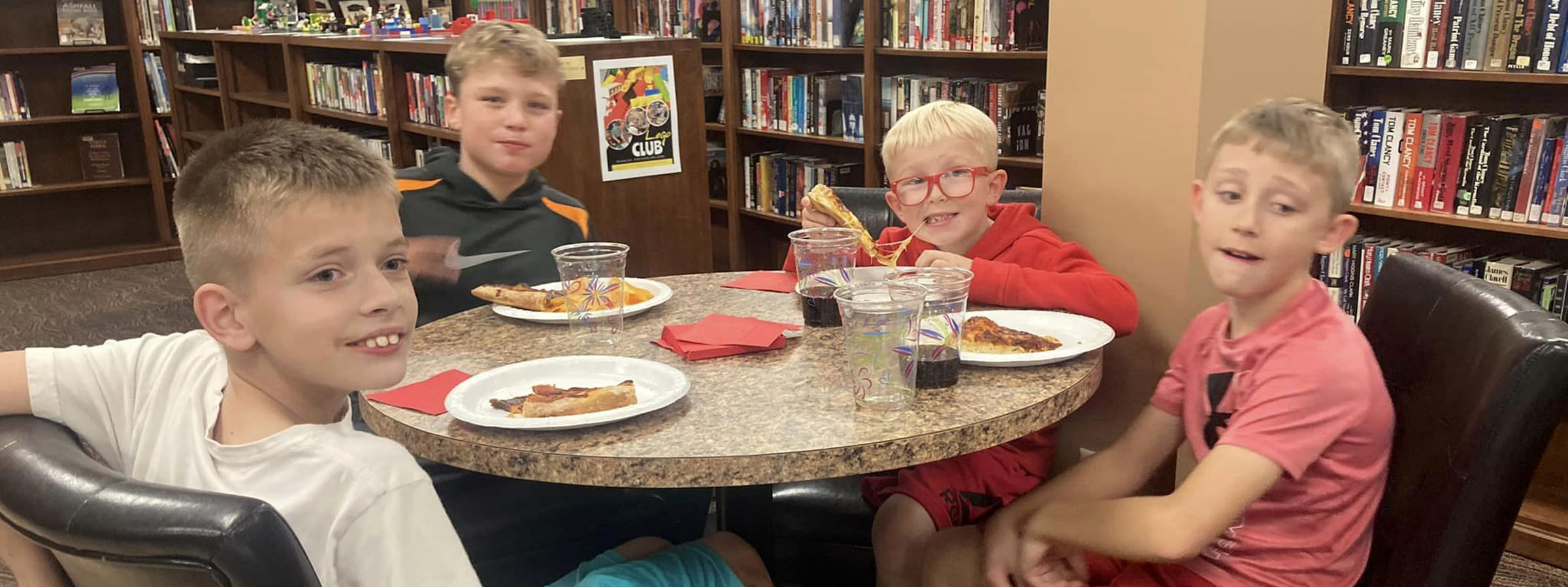 Three boys enjoying pizza at a library table.