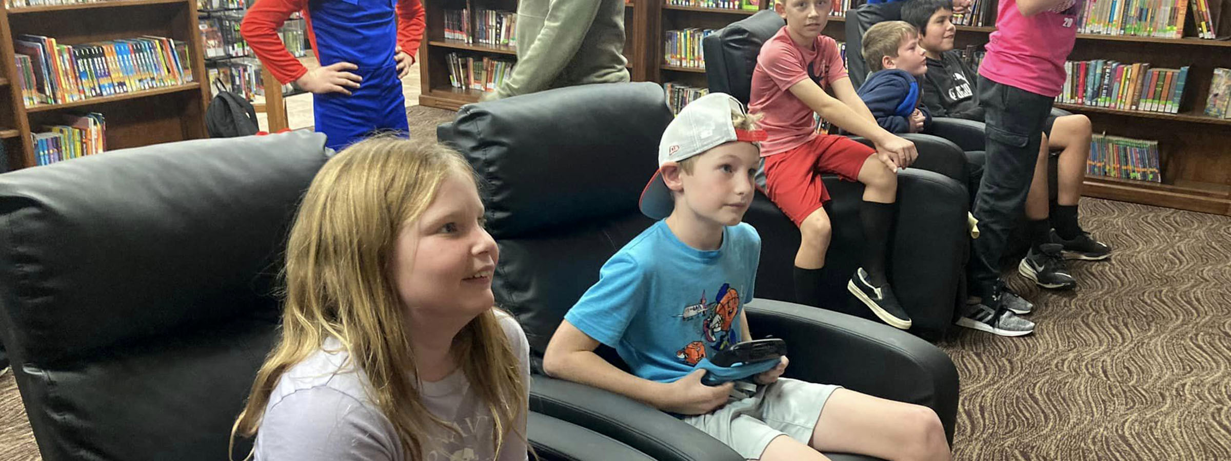 Children sitting in chairs in a library surrounded by books.