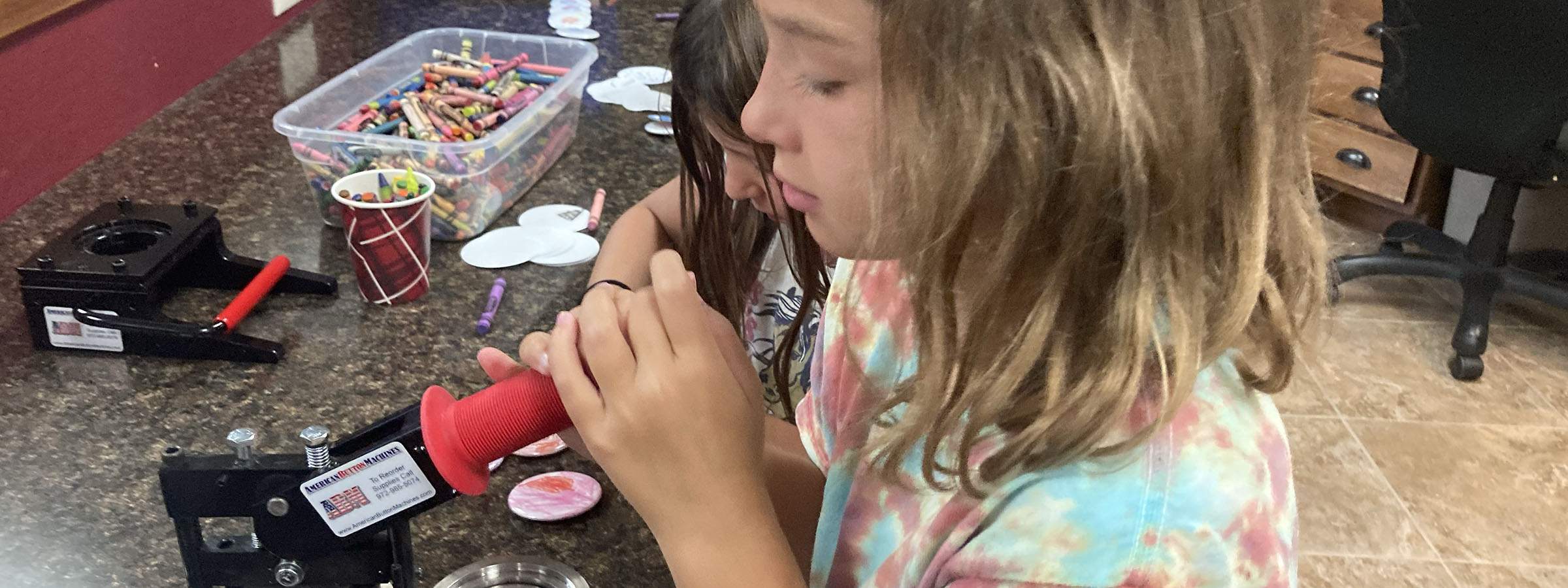 Two young girls joyfully operate a red candy-making machine, creating sweet treats together.