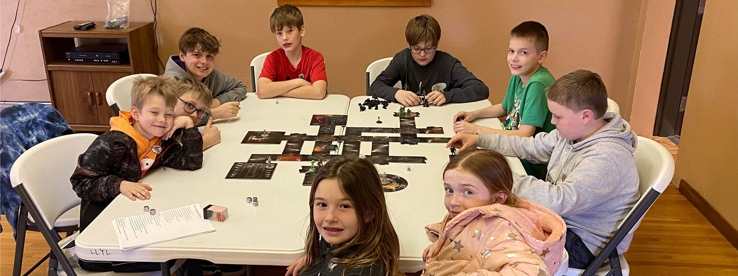 A group of kids sitting at a table with a man in the background.