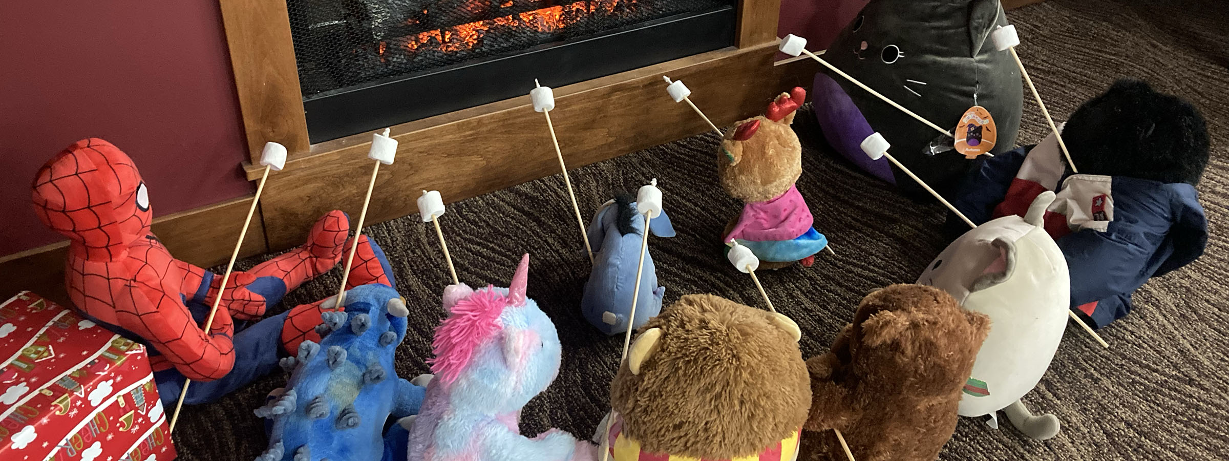  A cozy scene with stuffed animals gathered in front of a crackling fireplace.