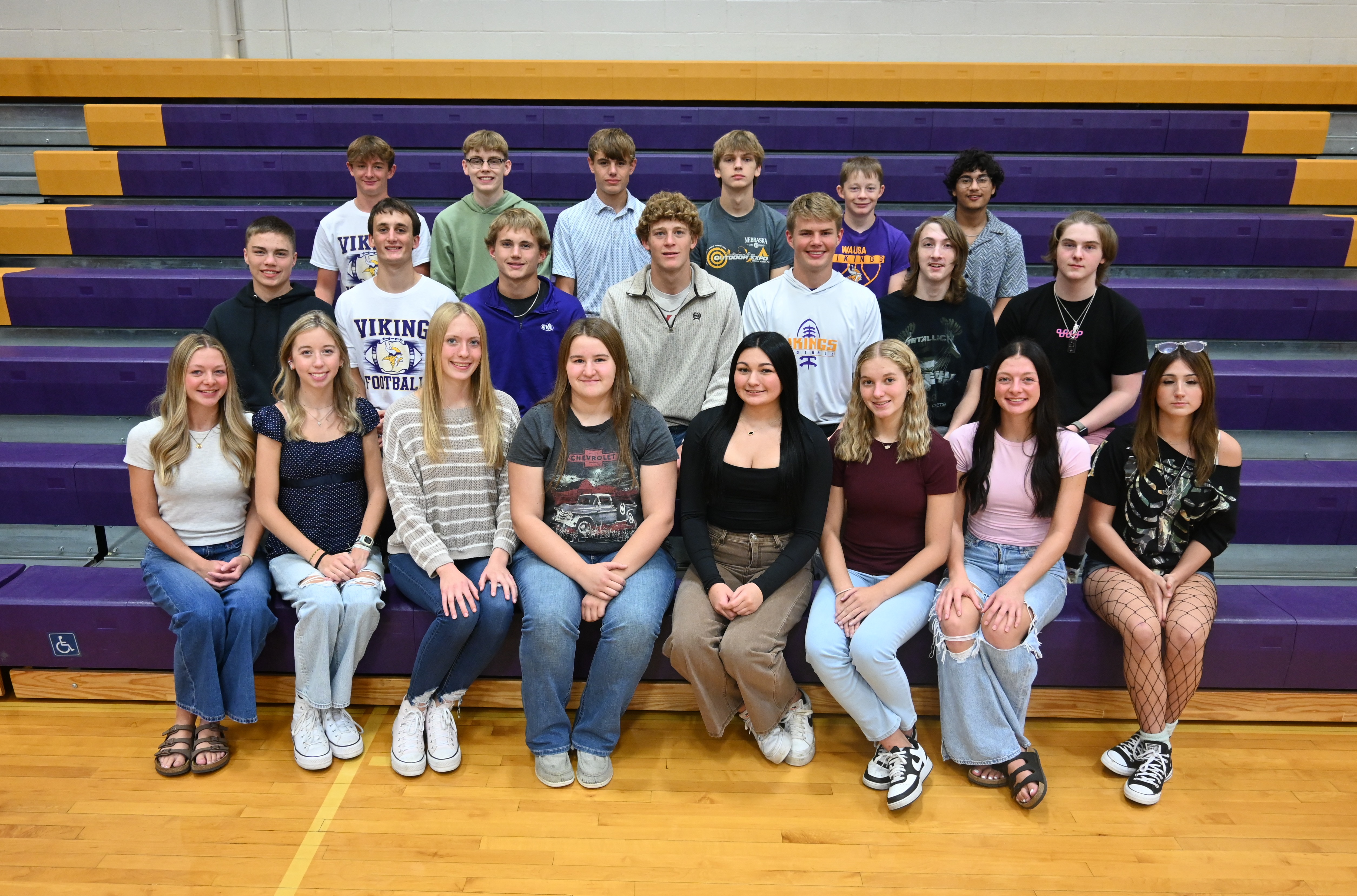 A group of young people sitting on bleachers in a gym.