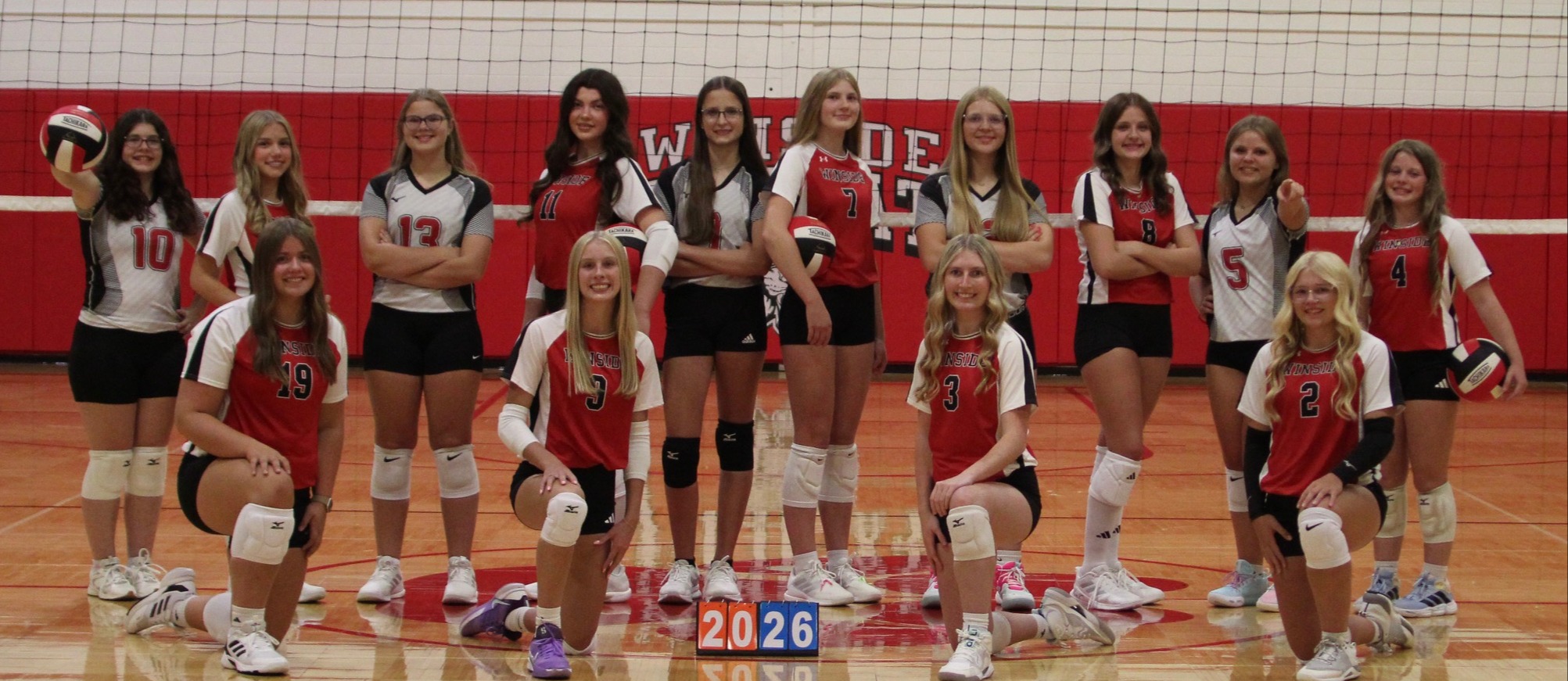 2026 Volleyball team of 14 players. 4 are kneeling and 10 are standing behind them in various poses
