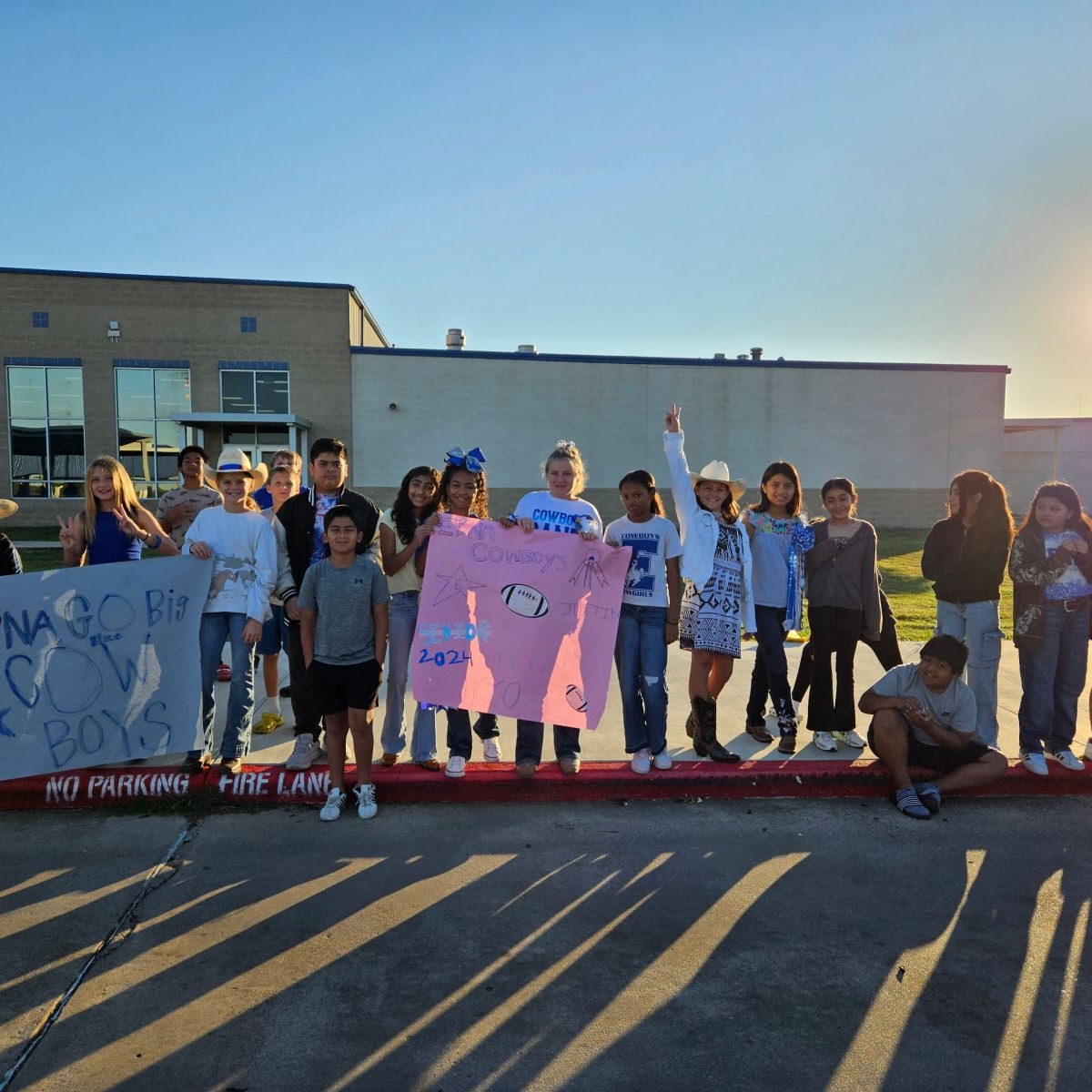 Students lined up on the sidewalk with signs to cheer on the football team