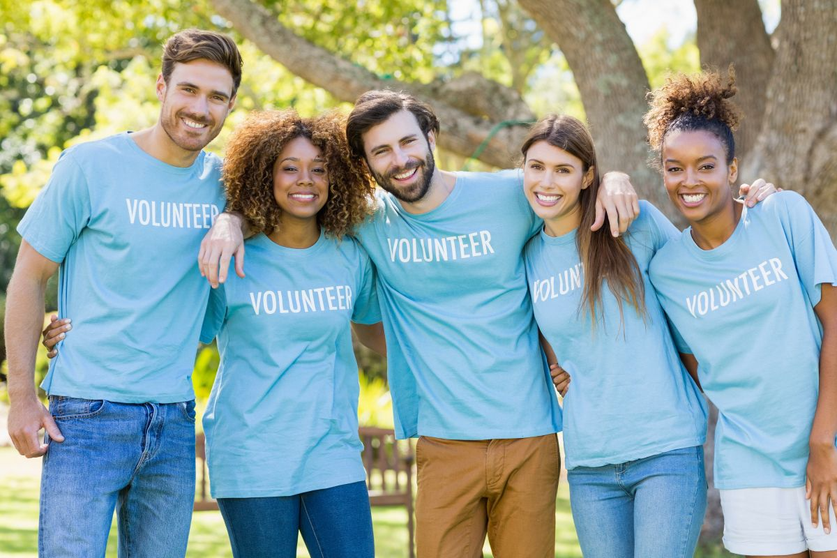 A diverse group of young volunteers proudly wearing matching shirts, smiling and ready to make a difference together.