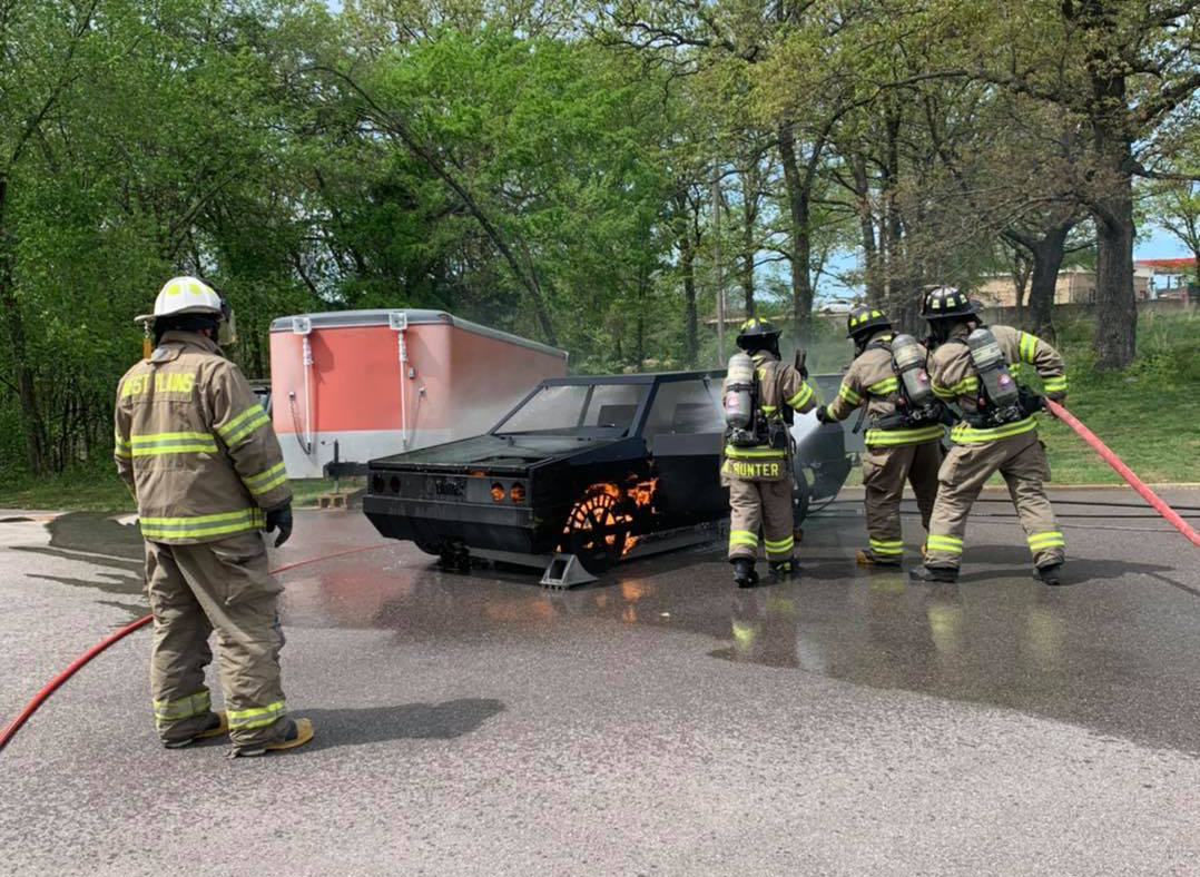 Firefighters are actively working on a car in a parking lot