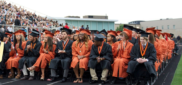 A joyful group of graduates in caps and gowns sitting together on bleachers, celebrating their graduation day.