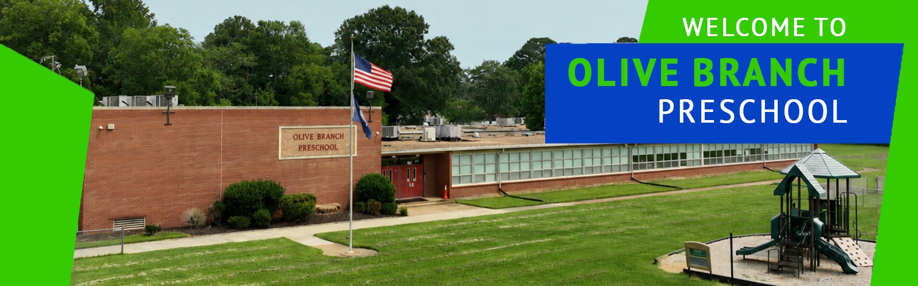 A building with a flagpole stands before a grassy field. Trees and a playground are in the background.