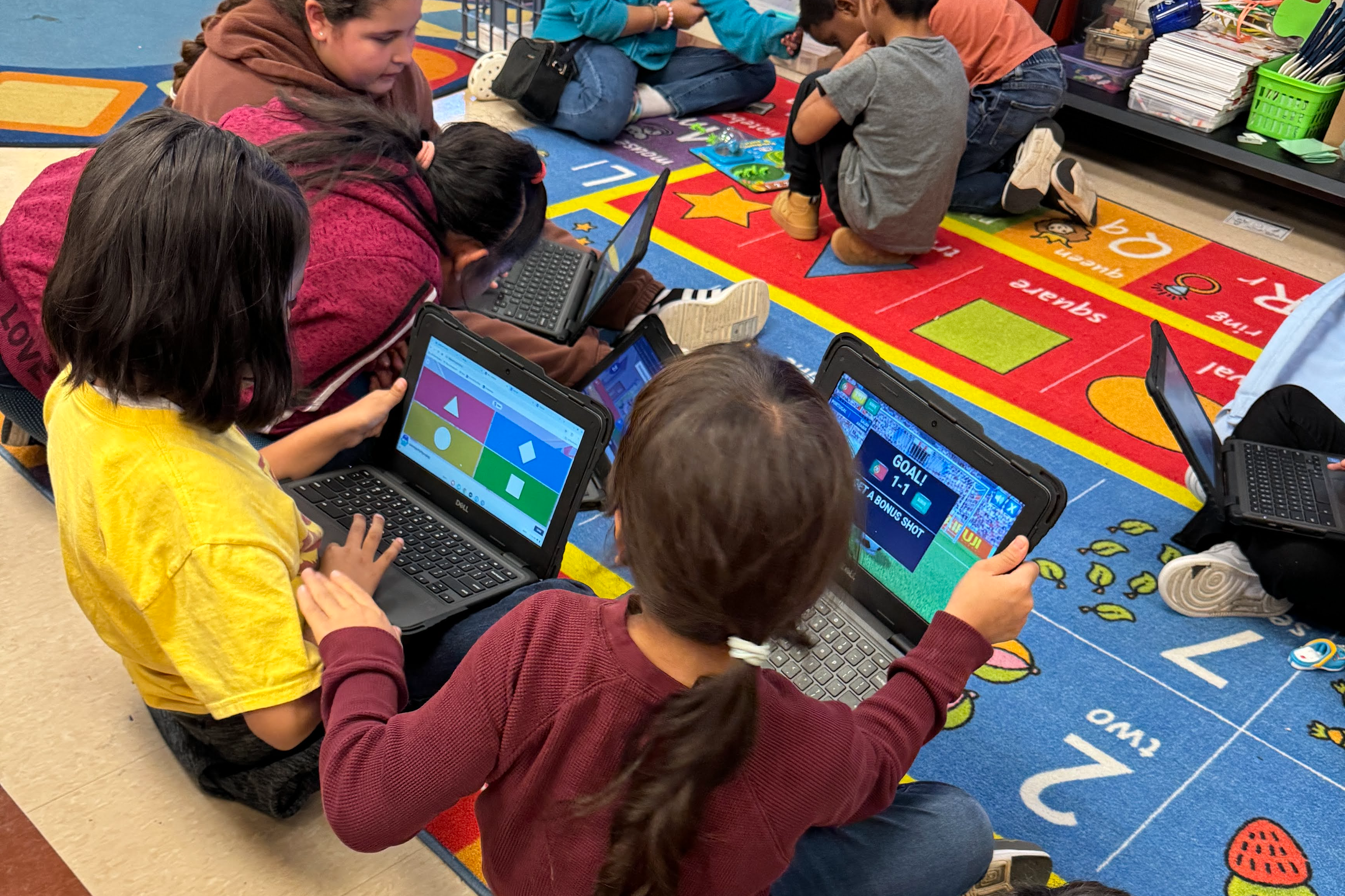 students sitting on the carpet while playing games on their Chromebooks