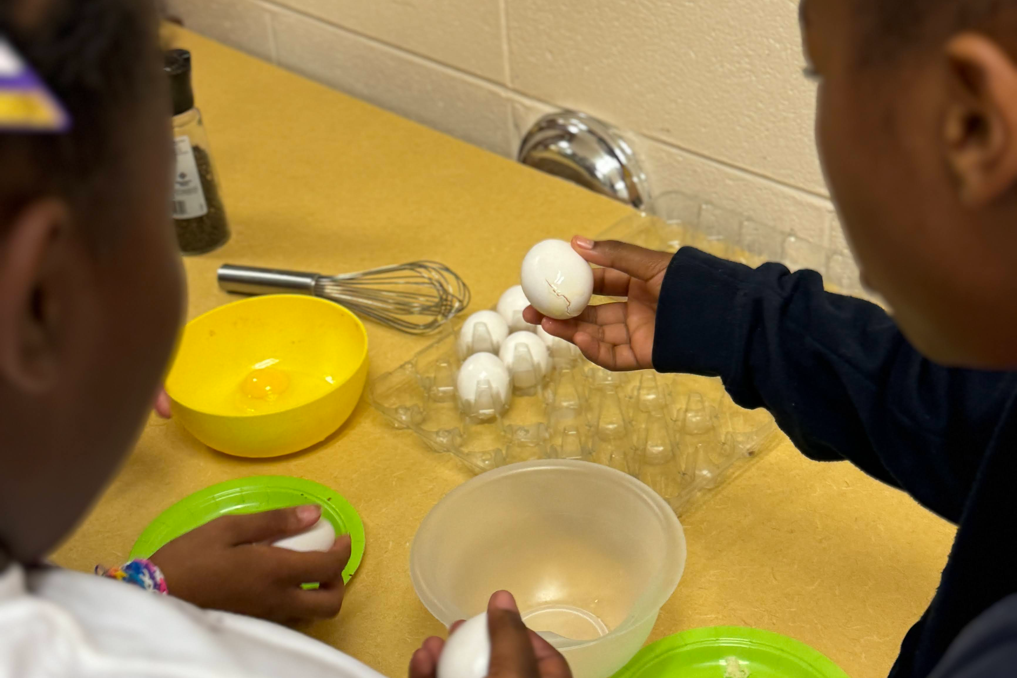 students standing next to a counter with eggs and kitchen utensils