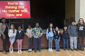 Two teachers and 8 students standing in front of the school stage.