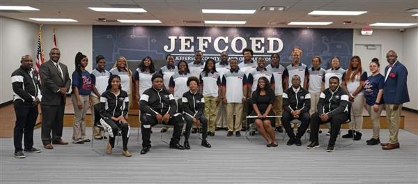 A group of individuals posing in front of a sign with the text 'JECOED'.