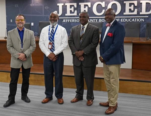 A group of men standing in front of a plaque with the word "JEFOED" on it.