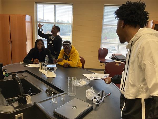 Students gathered around a science lab, observing and discussing an experiment.