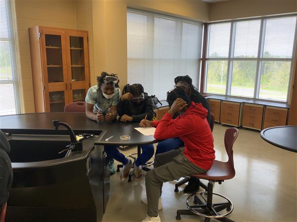 A group of people gathered around a table, with some using virtual reality headsets.