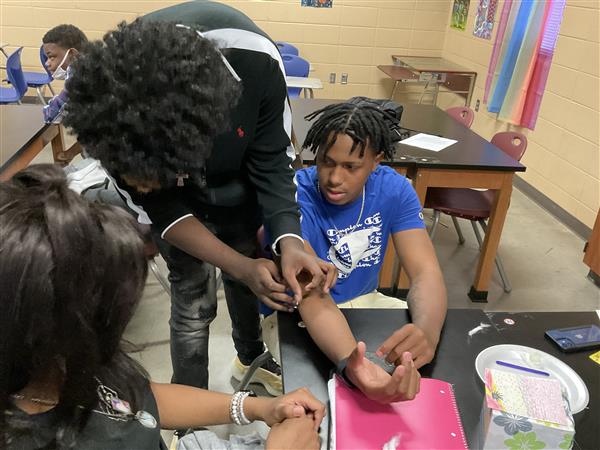 Three young people engaged in a hands-on learning activity, with one individual observing and possibly assisting.