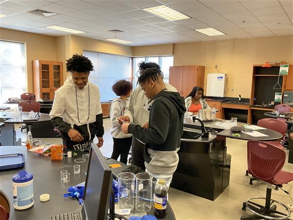 Three people in a lab, one of whom is pouring water from a bottle into a test tube.