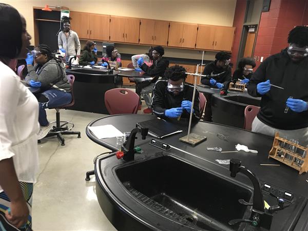 A science lab with people engaged in experiments, featuring blue gloves and various equipment on the table.