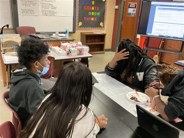 A classroom setting with students engaged in group work around a table.