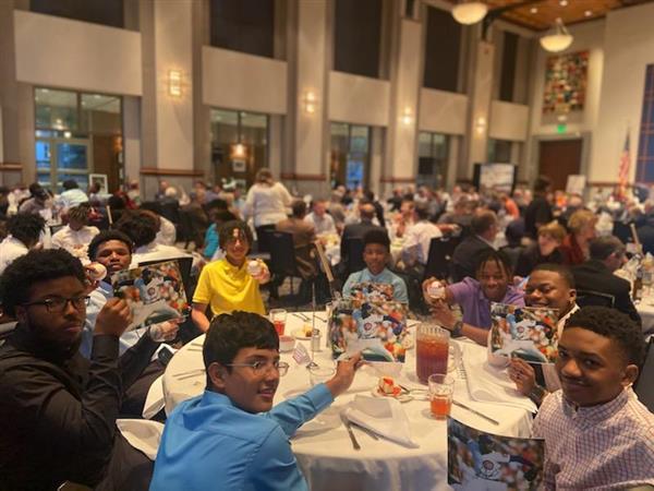 A group of people seated at tables in a spacious dining room, enjoying a meal together.