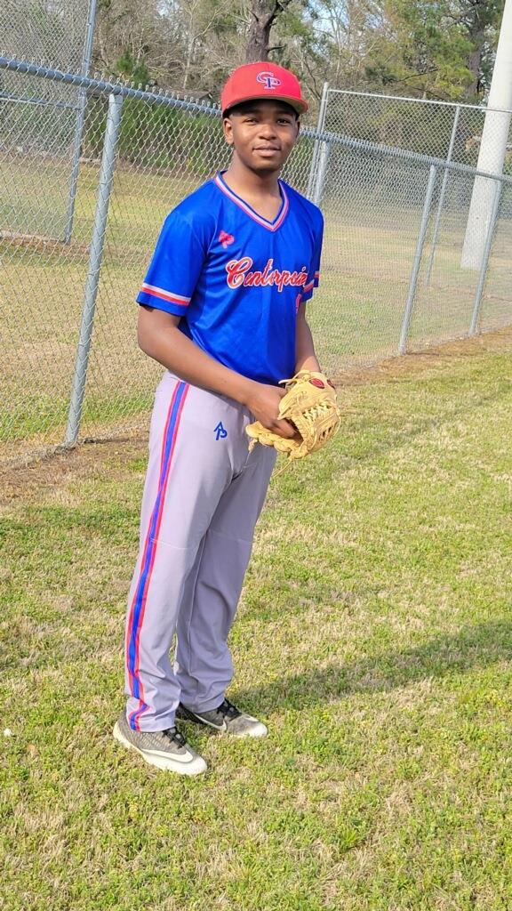 Baseball player in uniform with a baseball glove, standing on grass near a fence.