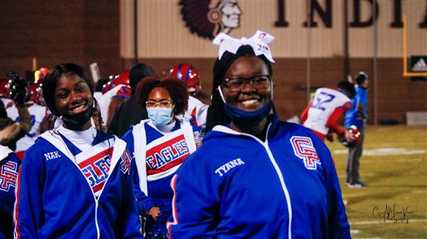 Two women in matching blue and white cheer uniforms, standing side by side on a football field.