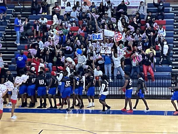 A group of people celebrating with signs and banners inside a basketball court.