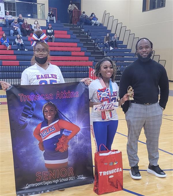 A group posing with a cheerleading sign, photo of a person in a cheer outfit, and a trophy.